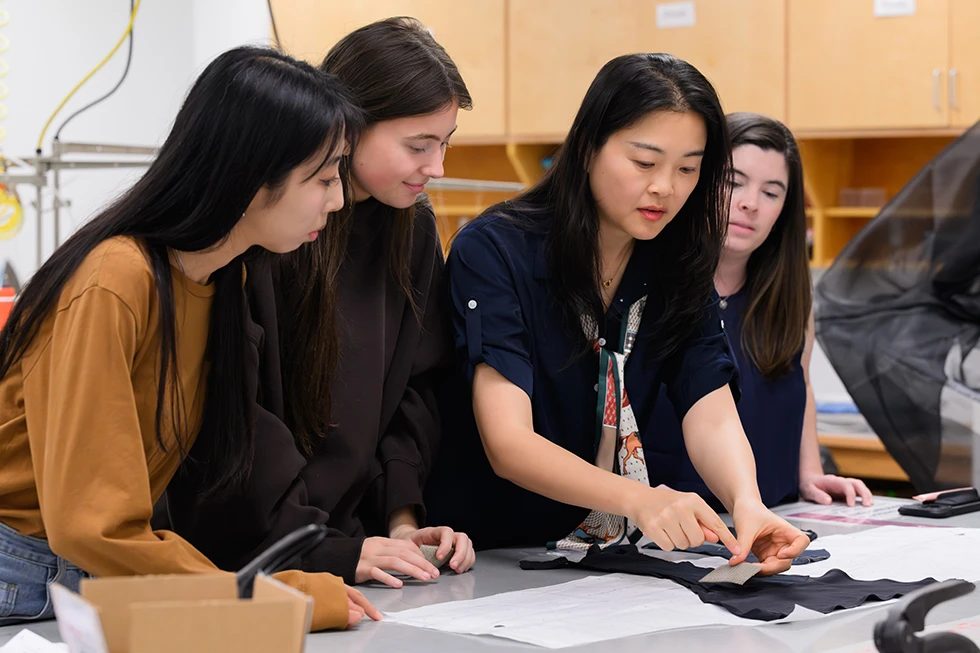 Students examine fabric samples together during a hands-on apparel design class.