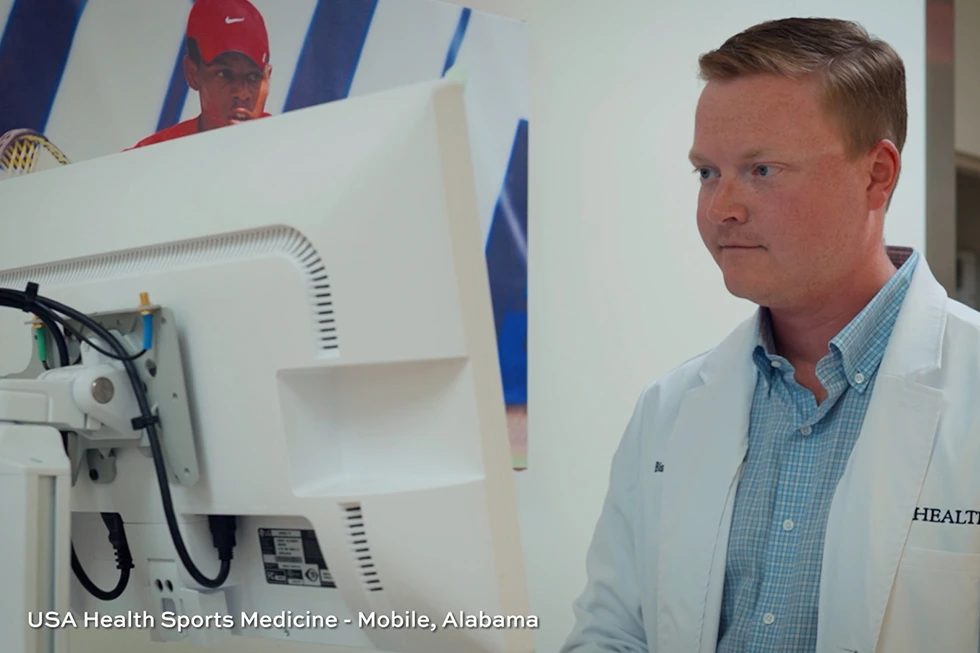 Sports medicine professional in a white coat reviews information on a computer monitor.