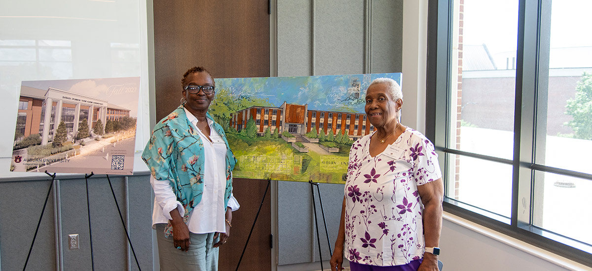 Two women stand next to easels displaying an architectural rendering and a painting of the Barbara Drummond Thorne Academic and Research Facility.