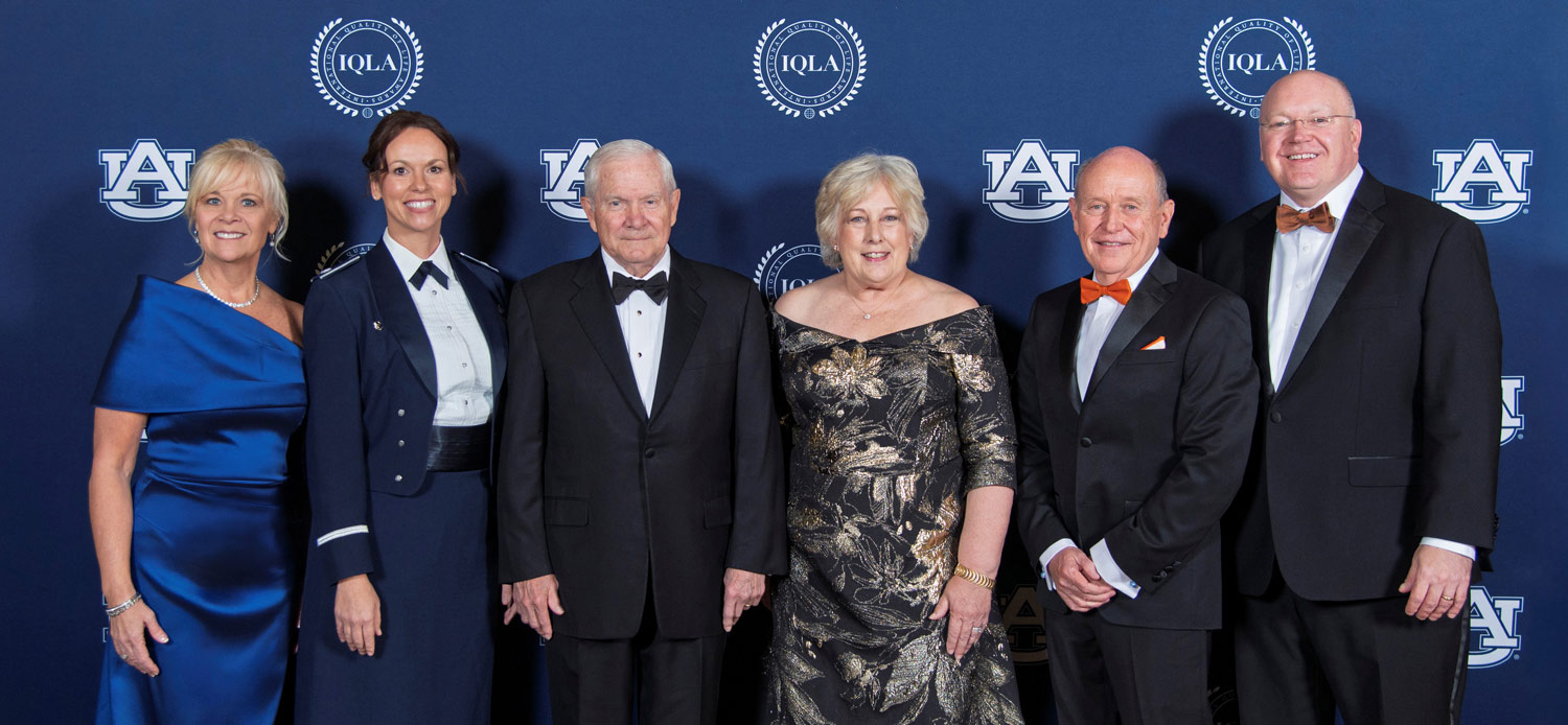 Six people in formal wear and military uniform pose in front of a blue Auburn University and IQLA branded backdrop.