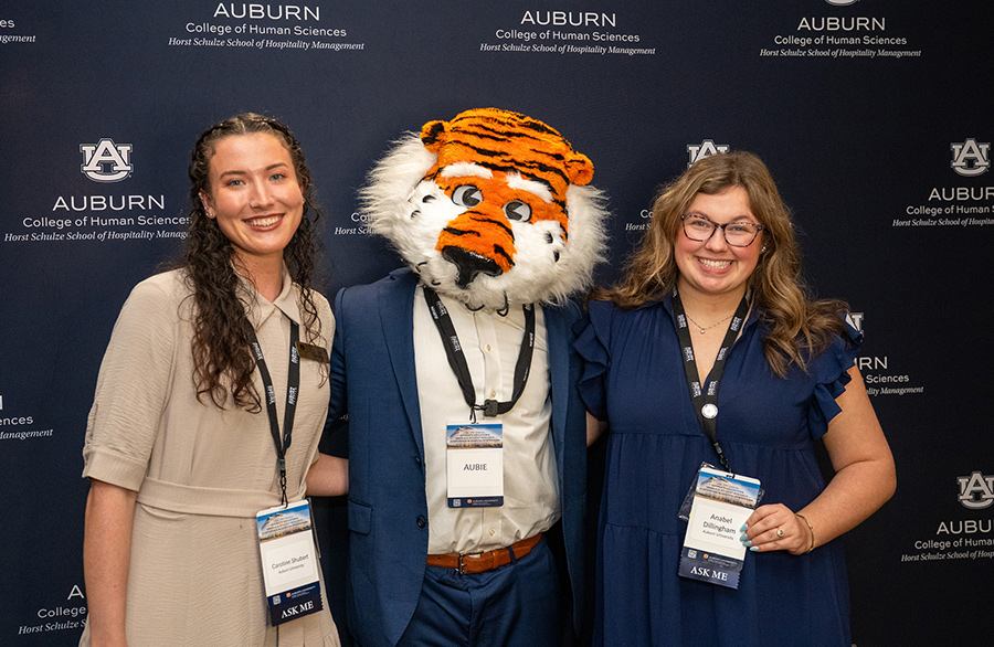 Two students and Auburn mascot Aubie smiling in front of a school backdrop.